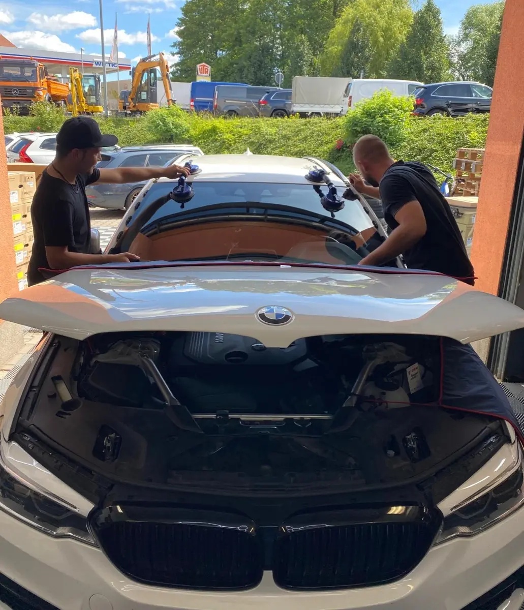 Zwei Mitarbeiter heben Frontscheibe auf BMW - Teamarbeit beim Scheibeneinbau