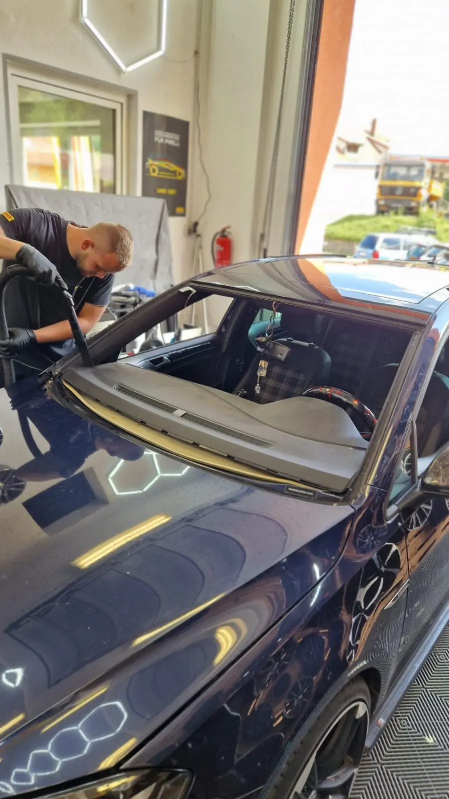 Mitarbeiter entfernt alte Windschutzscheibe aus VW Golf